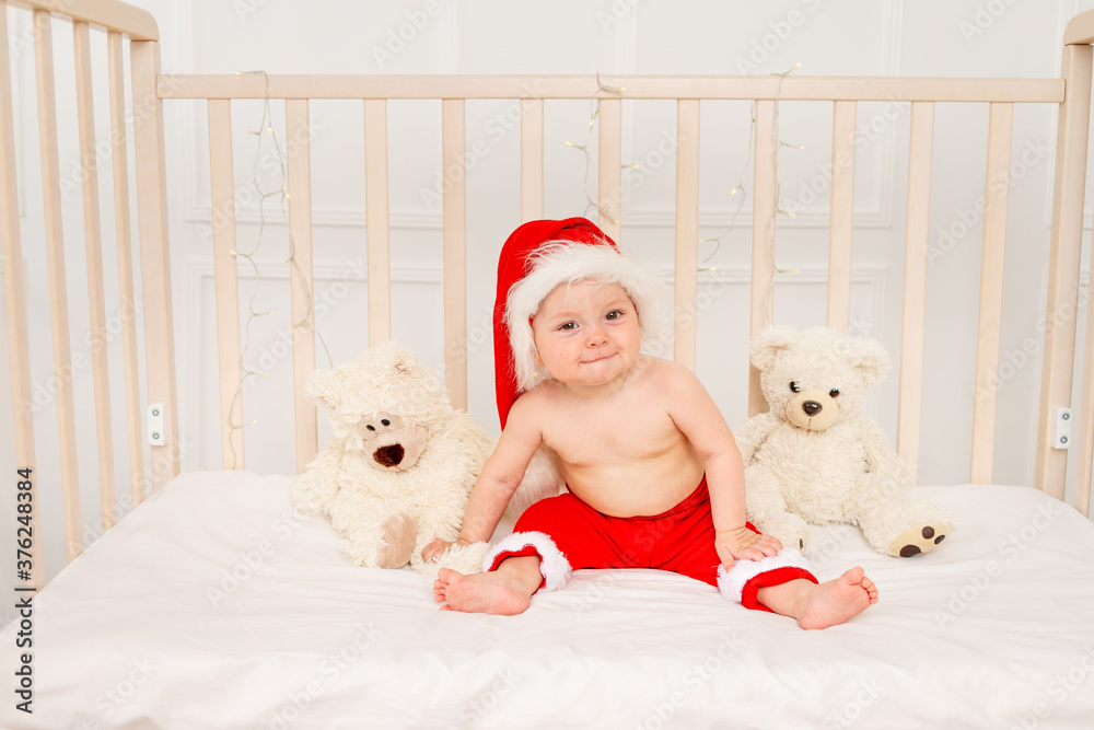 Obraz premium a small child is sitting in a crib in a Santa hat with stuffed toys bears, happy new year 2021, space for text