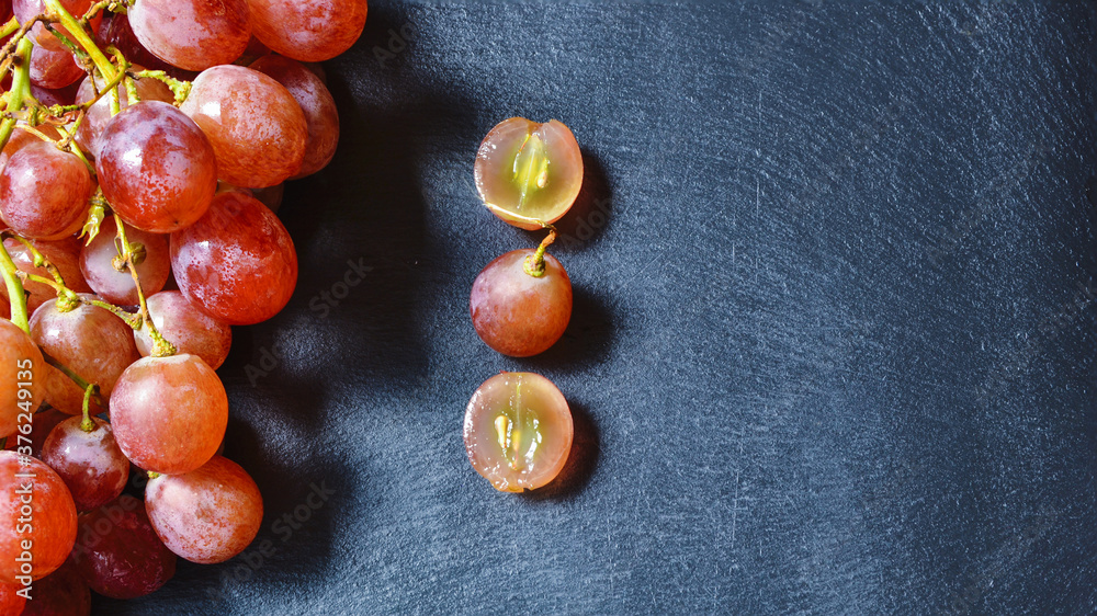 Obraz premium Uvas moradas sobre un plato de pizarra negra, bajo lo rayos del sol. Las primeras uvas de la temporada. Principios de otoño