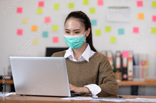 Happy Asian business woman wearing face mask looking laptop working at modern office or Co-Working Space,Business Startup Concept