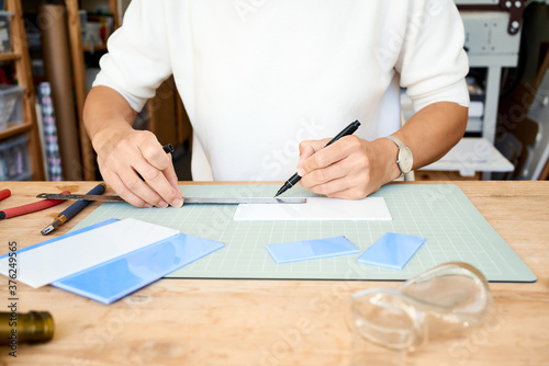 Faceless female entrepreneur cutting glass in artisan workroom. Business woman draws line on plate, having hobby, side hustle