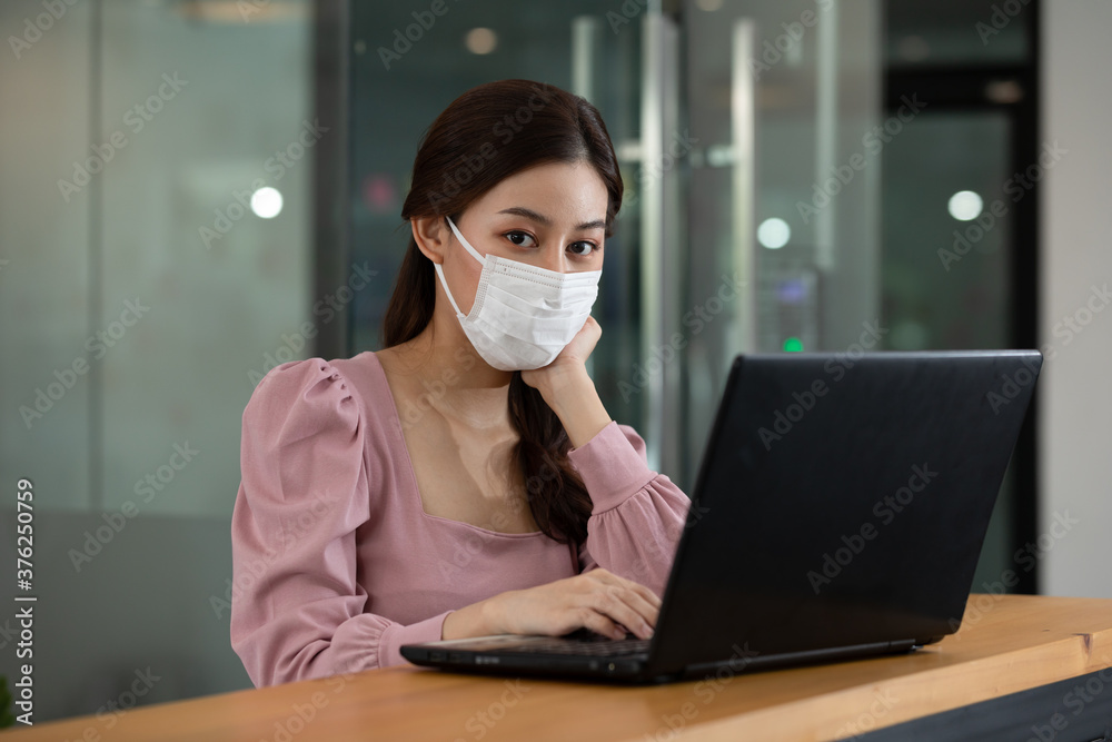 Happy Asian business woman wearing face mask looking laptop working at modern office or Co-Working Space,Business Startup Concept Happy Asian business woman wearing face mask looking laptop working at modern office or Co-Working Space,Business Startup Concept