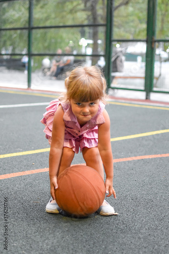 Funny little girl with a ball on the outdoor playground. Young cute sportswoman girl.
