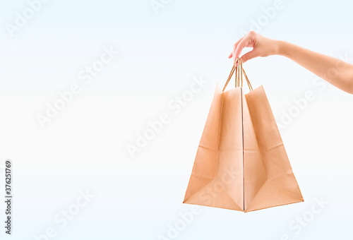 female hand holding paper bags on pale blue background