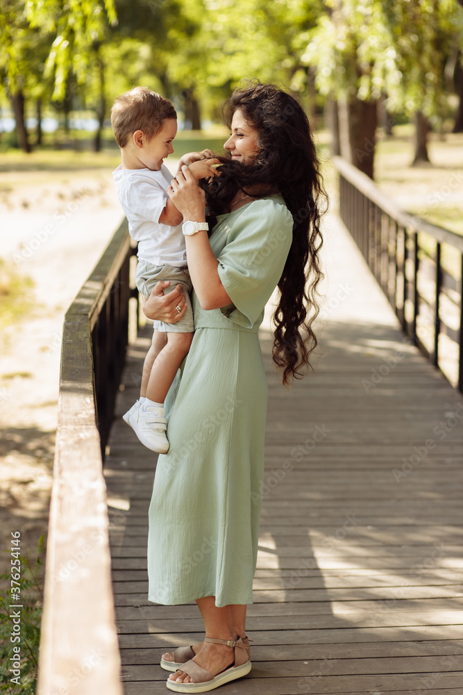 Adorable mother with joyful son at the park, beautiful woman hold in arms little boy, smiling, mommy plays with kid, enjoy family time, motherhood and childhood concept
