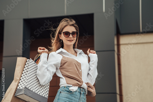 Portrait of european lady hold hand colorful bags woman after shopping in sunglasses white shirt jeans retail store near mall on the street sales black friday season bokeh background