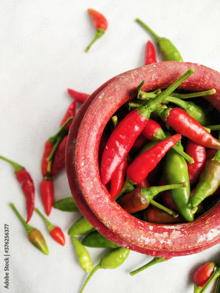 Red and Green chilli in a Red colored crock (mud made pot) in a white background Red and Green chilli in a Red colored crock (mud made pot) in a white background