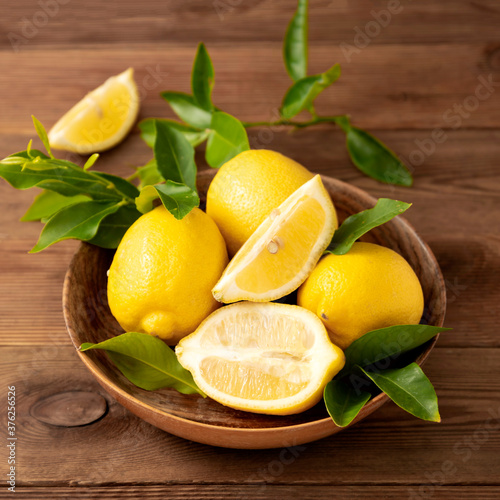Fototapeta Naklejka Na Ścianę i Meble -  Lemons on dark background in wooden bowl. Citrus fruits with leaves. Square image.