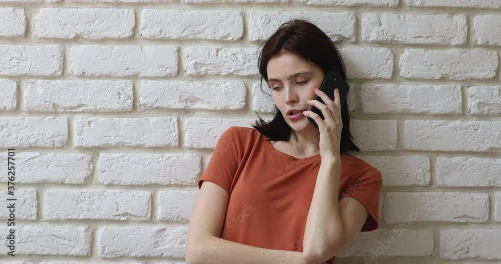 Young woman standing indoors leaned against white brick studio textured wall holding smart phone enjoy remote talk with friend. Generation and modern wireless technology easy convenient usage concept Young woman standing indoors leaned against white brick studio textured wall holding smart phone enjoy remote talk with friend. Generation and modern wireless technology easy convenient usage concept
