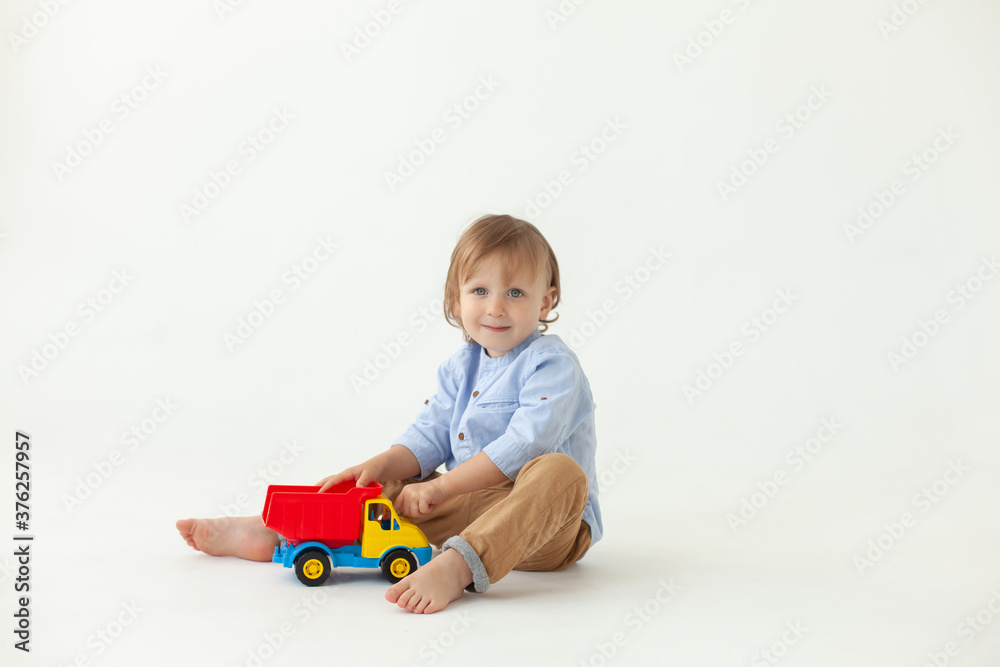 cute boy 2 years old sitting on the floor on a white background and playing with a toy car cute boy 2 years old sitting on the floor on a white background and playing with a toy car