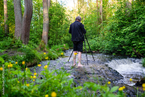 Barefoot photographer taking picture of water cascade while standing in river. Spring May day. Poland, Europe. photo