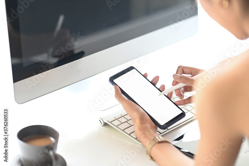 Closeup woman holding creative pen and mockup smartphone with empty screen on workspace.