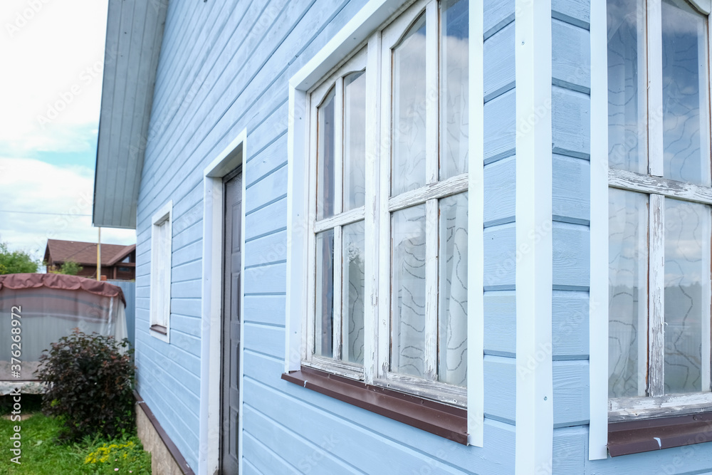 Small tiny wooden frame house painted in blue and white windows and door as a country residence in sunny summer day