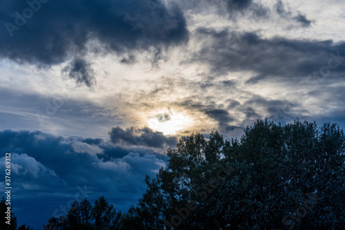 A dramatic sunset with the bright yellow sun breaking through the in the clouds in a blue stormy sky