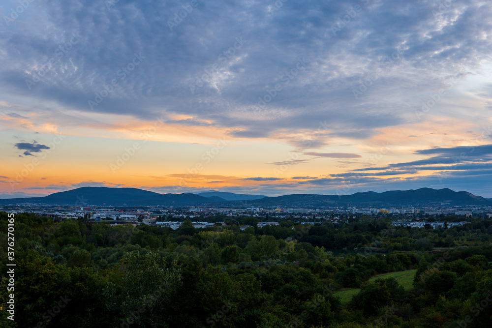 Striking orange sky with the sunset peaking through the clouds over Vienna Austria with a view of the city, green trees and mountains. Stunning view from high above.