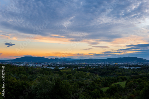 Striking orange sky with the sunset peaking through the clouds over Vienna Austria with a view of the city, green trees and mountains. Stunning view from high above.