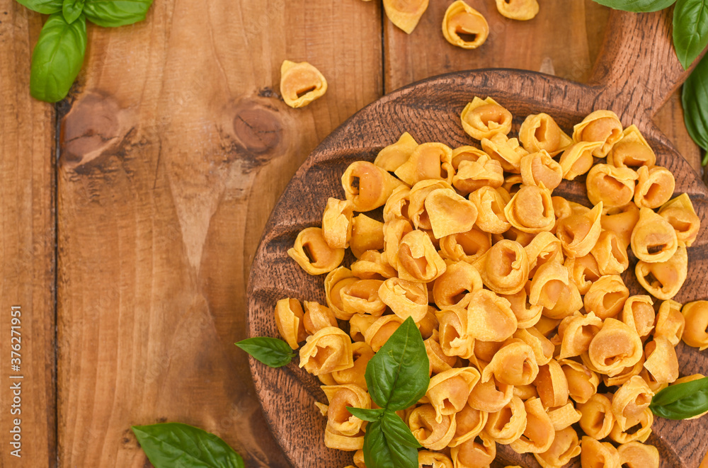 Tortellini mignon on a wooden board with basil and parmesan. Specialties of the cuisine from Bologna and Emilia Romagna: Cappelletti, fresh egg pasta with meat and vegetables filling. Copy space