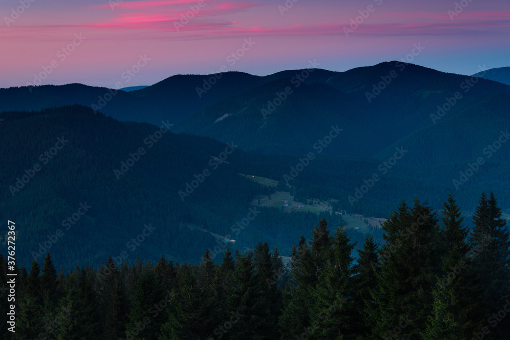 Amazing landscape in the layers of mountains at the dusk. View of colorful sky and hills covered by forest. 