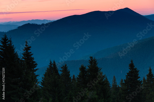 Amazing landscape in the layers of mountains at the dusk. View of colorful sky and hills covered by forest. 