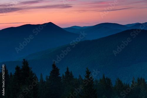 Amazing landscape in the layers of mountains at the dusk. View of colorful sky and hills covered by forest.
