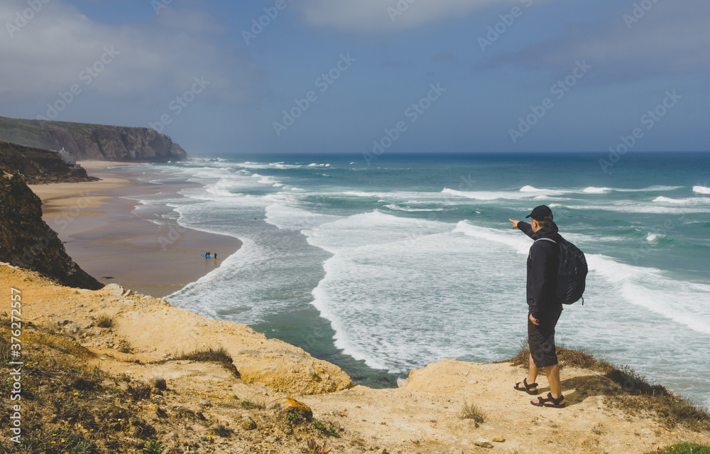 A tourist on a rocky shore looks in the distance at the raging ocean and surfers. Atlantic Ocean. Portugal. A tourist on a rocky shore looks in the distance at the raging ocean and surfers. Atlantic Ocean. Portugal.