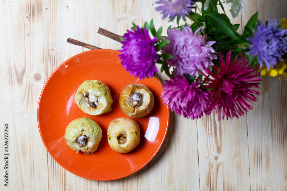 baked apples with walnut and sugar on orange plate on wooden table with cinnamon and aster flowers baked apples with walnut and sugar on orange plate on wooden table with cinnamon and aster flowers