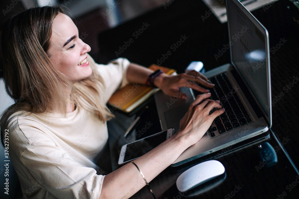 Young slender girl at the restaurant table works behind a laptop