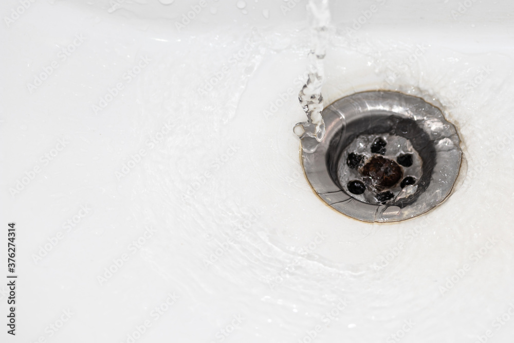 Close up a stream of clean water flows into the sink sewer hole. A jet of water flows into the drain enamel sink. Close up a stream of clean water flows into the sink sewer hole. A jet of water flows into the drain enamel sink.