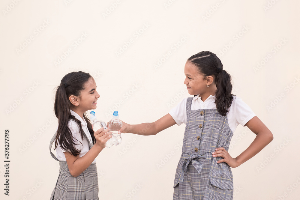 Little girls wearing water bottle toasting and looking each other. Concept of fellowship on school. Little girls wearing water bottle toasting and looking each other. Concept of fellowship on school.