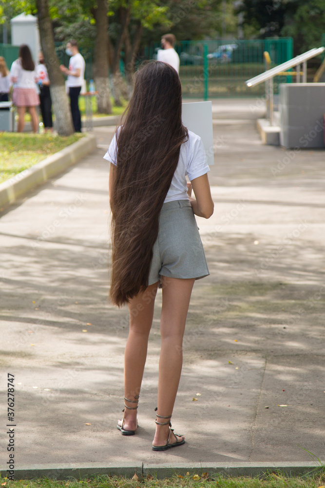 A girl with very long hair is standing on the street.