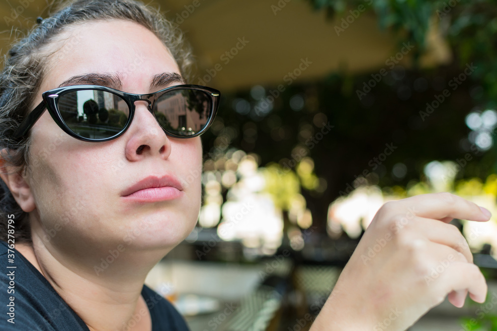 Portrait of young woman with sunglasses, serious, waiting, sitting in an outdoor bar. Portrait of young woman with sunglasses, serious, waiting, sitting in an outdoor bar.
