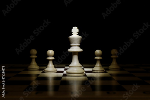 chess pieces on chessboard on black background. king and his pawns