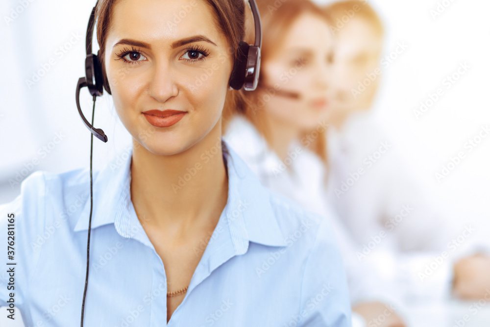Call center operators. Focus on beautiful business woman using headset in sunny office Call center operators. Focus on beautiful business woman using headset in sunny office