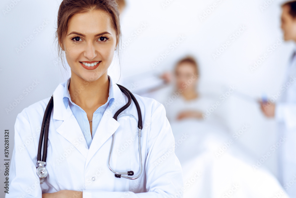 Female doctor smiling on the background with patient in the bed and two doctors Female doctor smiling on the background with patient in the bed and two doctors