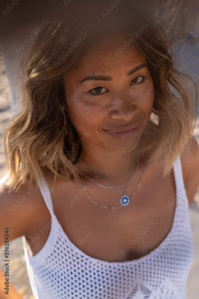 Close up portrait of a young beautiful Thai woman wearing a wooden hat and stylish necklace relaxing alone on the beach near the Atlantic Ocean. Woman's freedom lifestyle concept. Lisbon, Portugal Close up portrait of a young beautiful Thai woman wearing a wooden hat and stylish necklace relaxing alone on the beach near the Atlantic Ocean. Woman's freedom lifestyle concept. Lisbon, Portugal