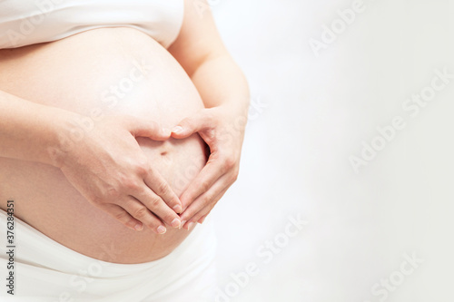 Pregnant woman hold heart-shaped hands on her baby bumps skin. Copyspace for your text.