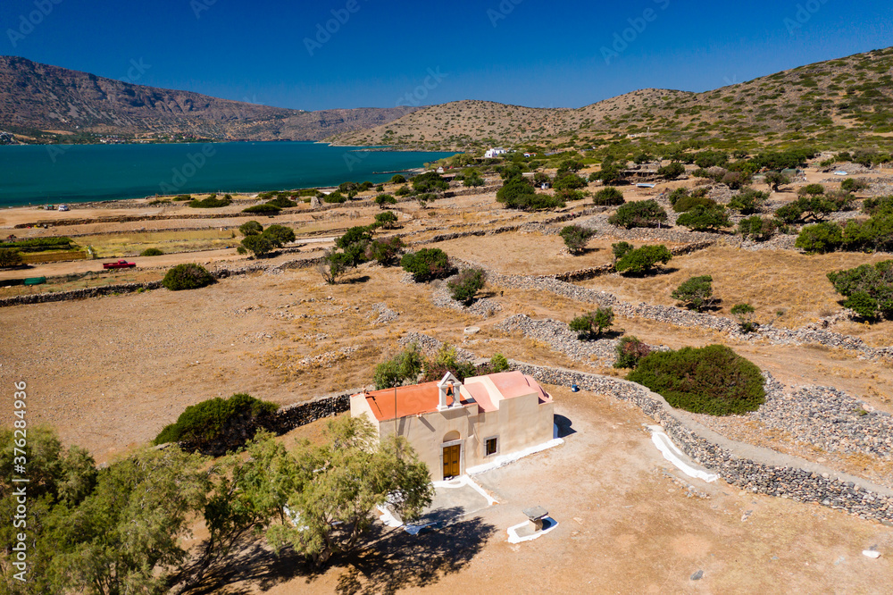 Aerial view of a small church next to a blue ocean on a hot Greek island (Ascension Church, Elounda, Crete)