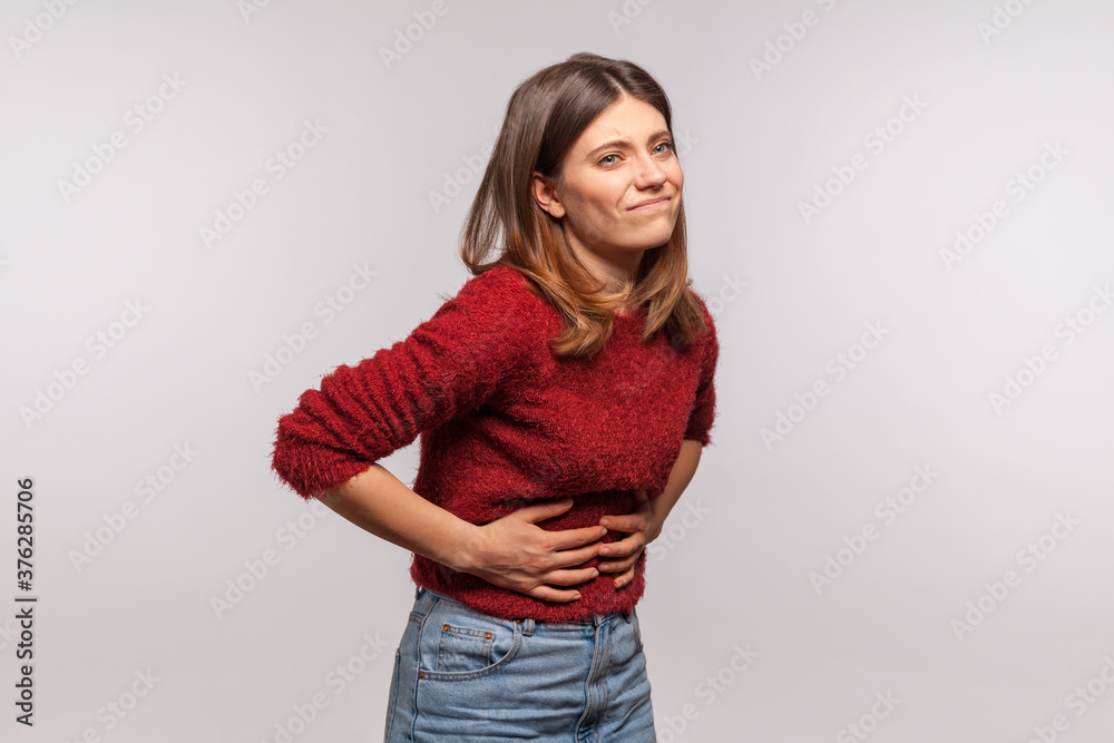 Girl in shaggy sweater touching belly, grimacing from stomach ache, severe abdominal distress, symptoms of constipation, indigestion, gastrointestinal disorder. studio shot isolated on gray background Girl in shaggy sweater touching belly, grimacing from stomach ache, severe abdominal distress, symptoms of constipation, indigestion, gastrointestinal disorder. studio shot isolated on gray background