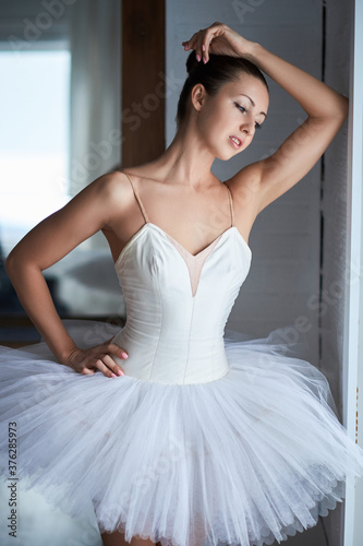 Side view of beautiful ballerina standing and looking through window. Copyspace