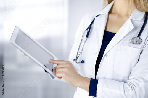 Unknown woman-doctor is holding a tablet computer in her hands,while standing in the cabinet in a clinic. Female physician,with a stethoscope, close-up. Perfect medical service in a hospital. Medicine