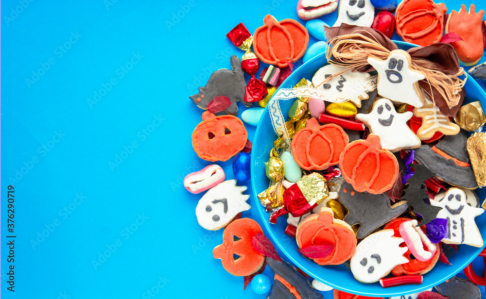 Fototapeta premium Halloween Jack o Lantern candy bowl with candy and halloween cookies Trick or Treat on blue background