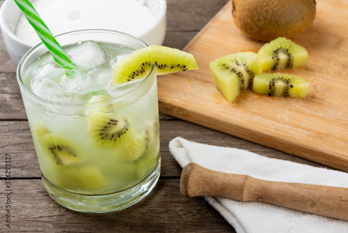 Brazilian kiwi caipirinha in a glass with ice with fruit slices over wooden board 