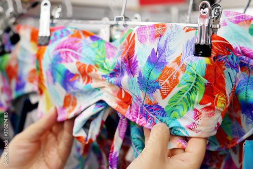 Woman chooses colorful swimsuit hanging on rack in lingerie store. Concept of shopping, customer during sale, female fashion for sea vacation