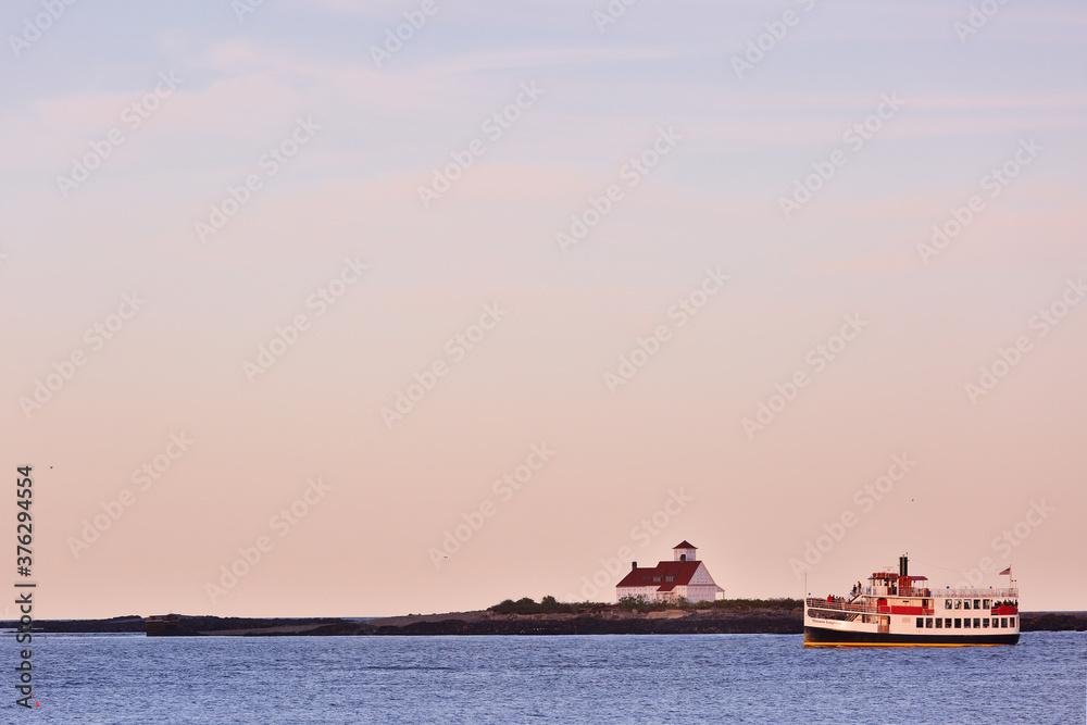 Fototapeta premium Beautiful Lighthouse Wood Island, Maine and Cruise boats at Sunset Viewing from Great Island Common state park, New Hampshire. 