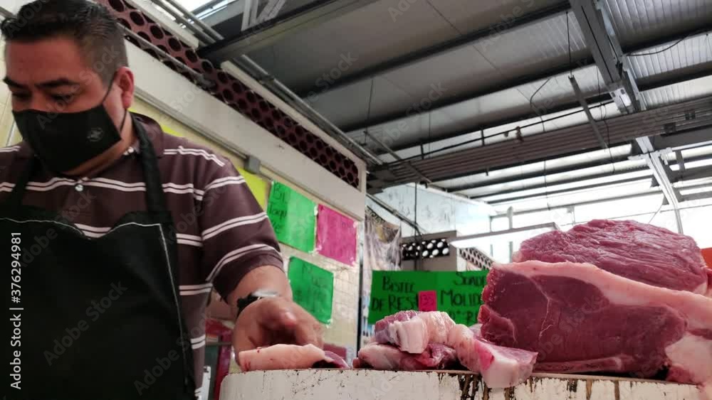 Carnicero con cubrebocas cortando la carne en el mercado 