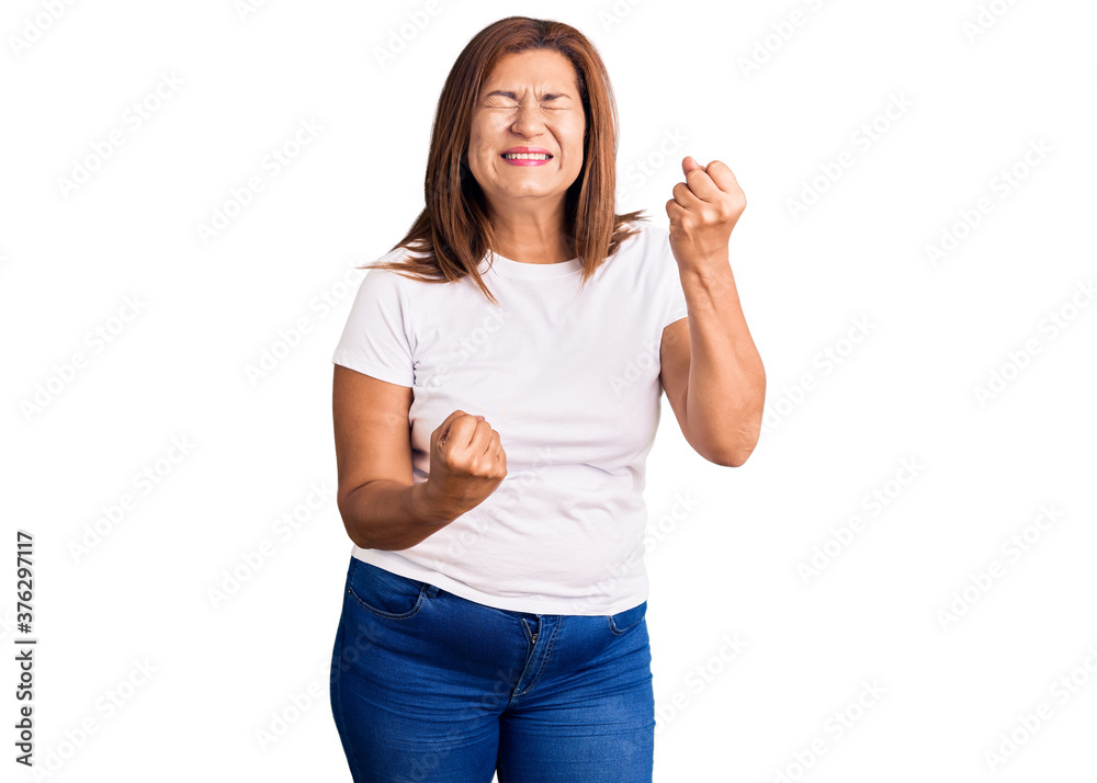 Middle age latin woman wearing casual white tshirt celebrating surprised and amazed for success with arms raised and eyes closed. winner concept. Middle age latin woman wearing casual white tshirt celebrating surprised and amazed for success with arms raised and eyes closed. winner concept.