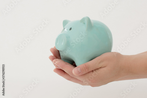 ew blue piggy bank in female hands on a white background. Horizontal photo. Concept - saving money, investing.