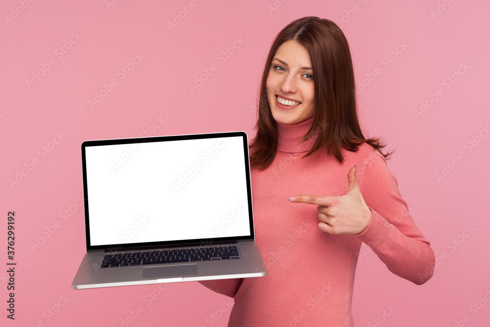 Brunette woman pointing finger at laptop with blank display she holding in hand, showing empty screen, bragging with internet advertisement. Indoor studio shot isolated on pink background Brunette woman pointing finger at laptop with blank display she holding in hand, showing empty screen, bragging with internet advertisement. Indoor studio shot isolated on pink background