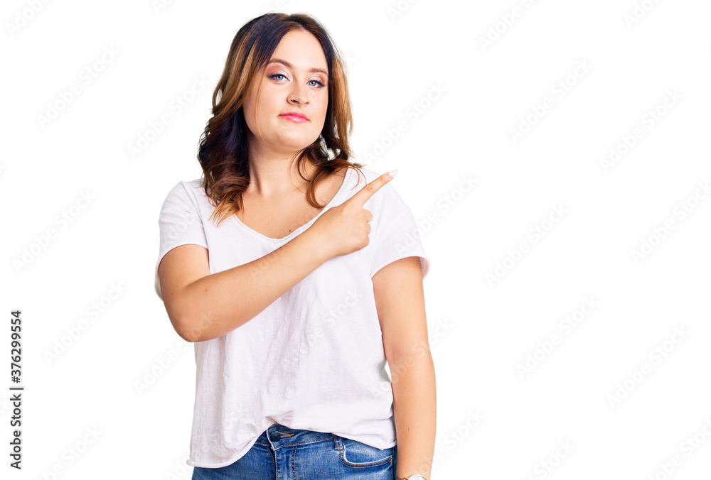 Young beautiful caucasian woman wearing casual white tshirt pointing with hand finger to the side showing advertisement, serious and calm face Young beautiful caucasian woman wearing casual white tshirt pointing with hand finger to the side showing advertisement, serious and calm face
