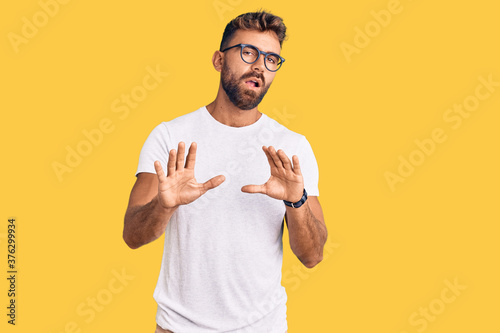 Young hispanic man wearing casual clothes and glasses moving away hands palms showing refusal and denial with afraid and disgusting expression. stop and forbidden.