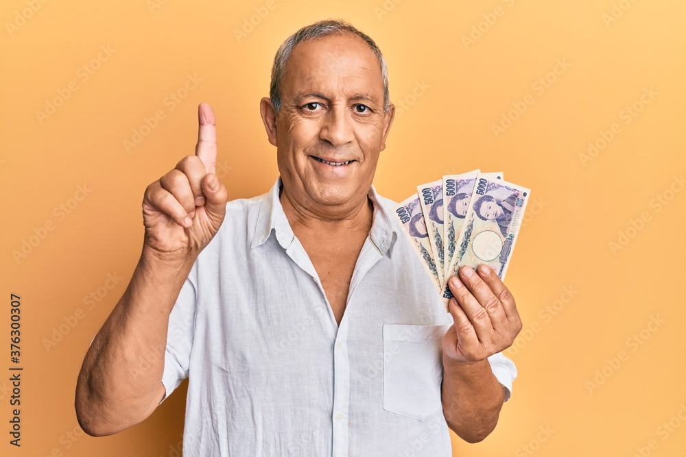 Handsome mature man holding 5000 japanese yen banknotes smiling with an idea or question pointing finger with happy face, number one Handsome mature man holding 5000 japanese yen banknotes smiling with an idea or question pointing finger with happy face, number one